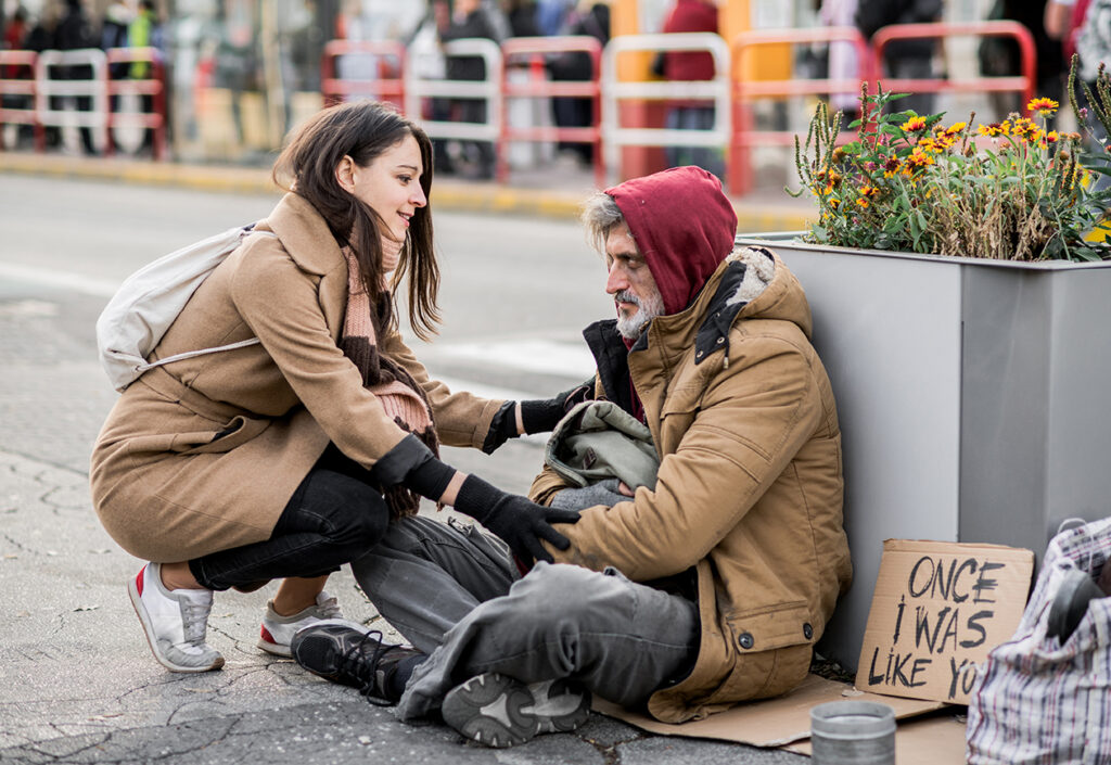 Woman Trying to Help Homeless Man sitting on city street.