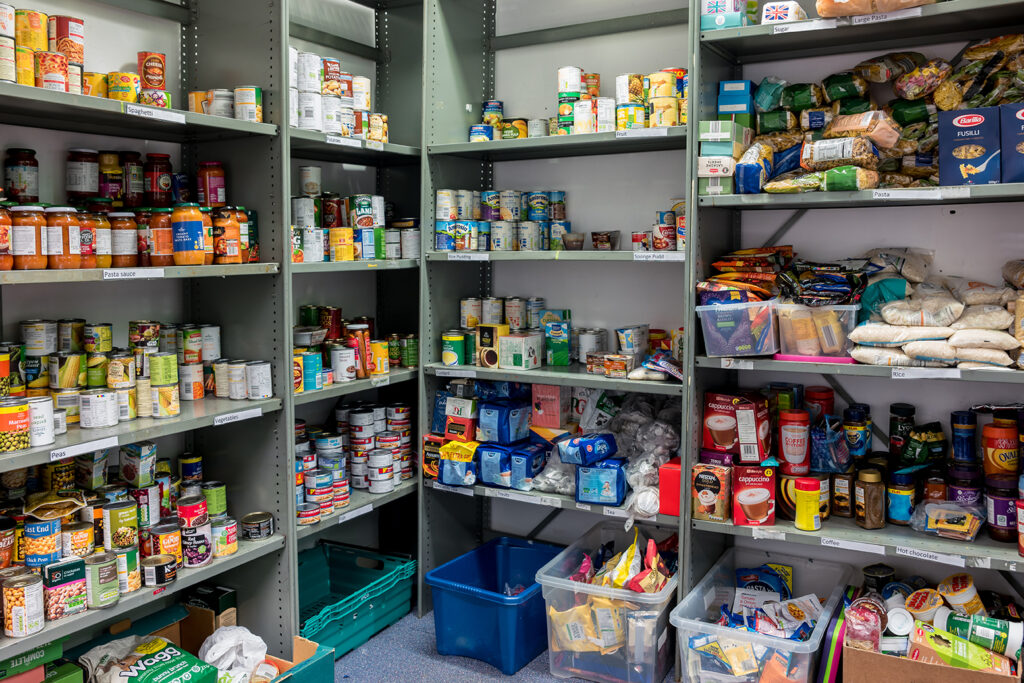 Storage shelves in a local church food bank warehouse showing a variety of tins and store cupboard essentials ready for food parcels