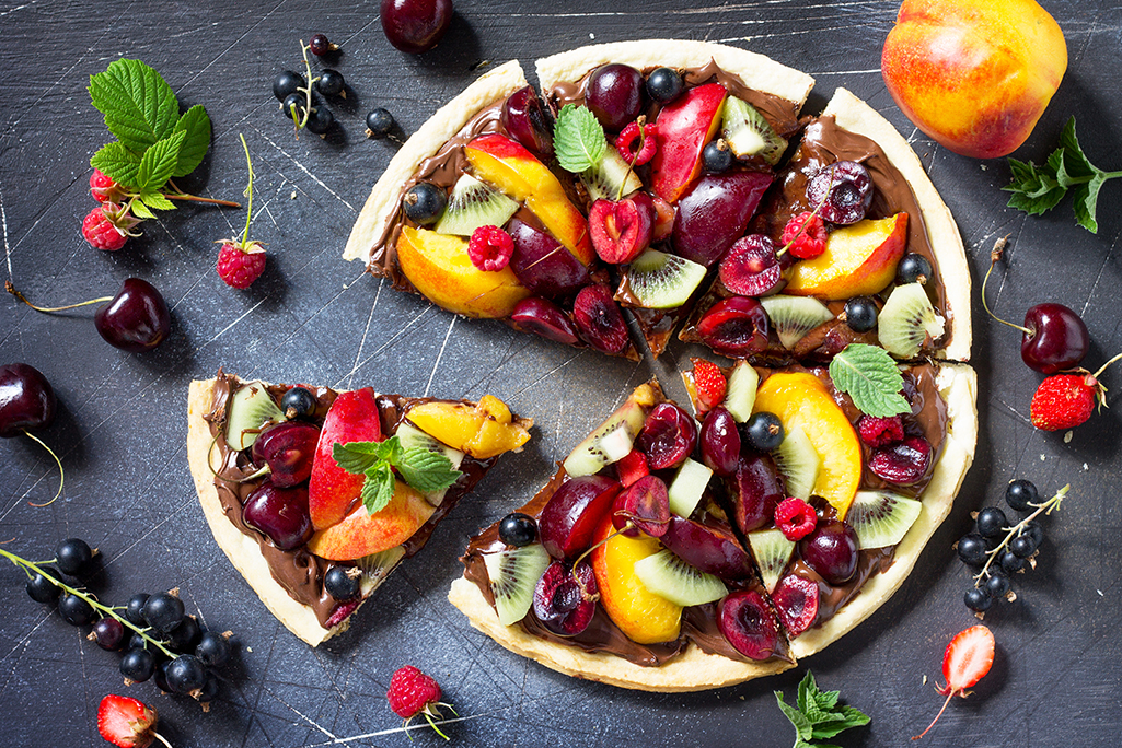 Vitamin dessert. Delicious homemade Summer fruit berry pizza with chocolate paste on a dark stone table. Top view flat lay background.