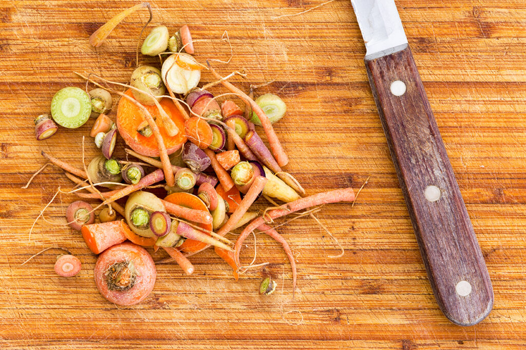Scraps leftover from cutting raw carrots beside knife over large wooden cutting board