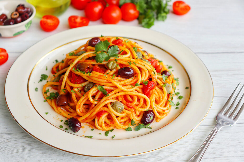 Italian Traditional Dish"Spaghetti alla Puttanesca",spaghetti with tomato sauce,anchovy,capers,olives,olive oil,peppers and parleys on plate with white wood table background.Simple and easy recipe
