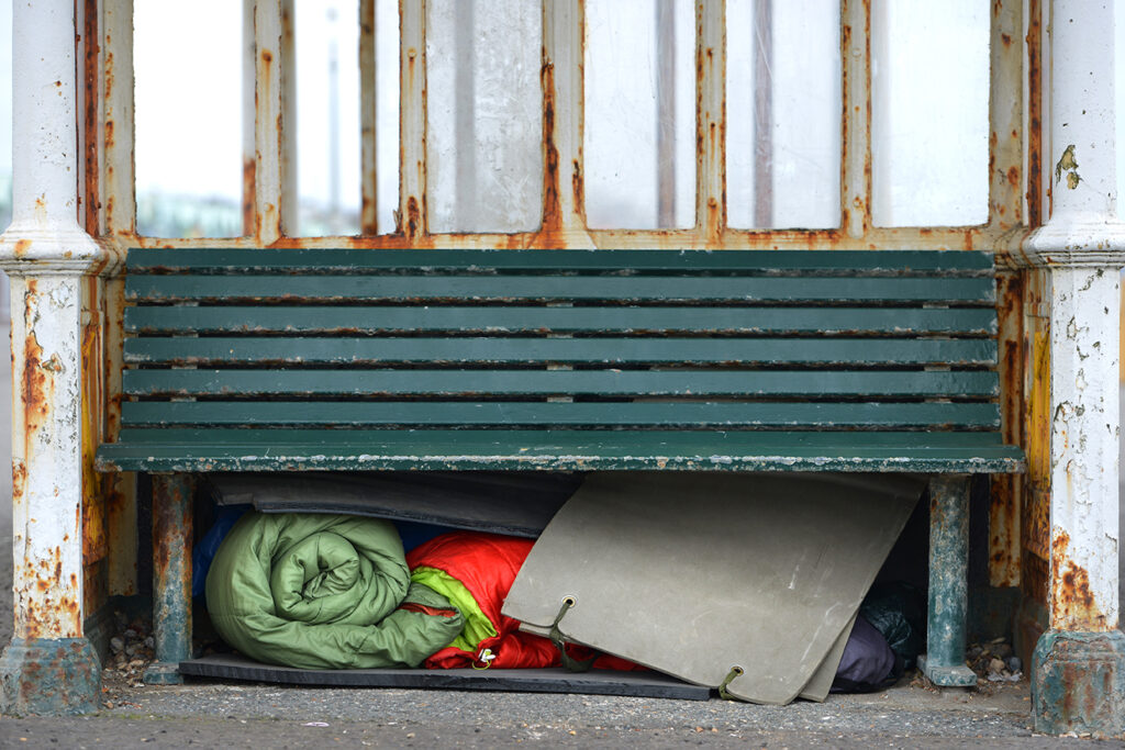 Homeless person's sleeping bags and bedding under a bench